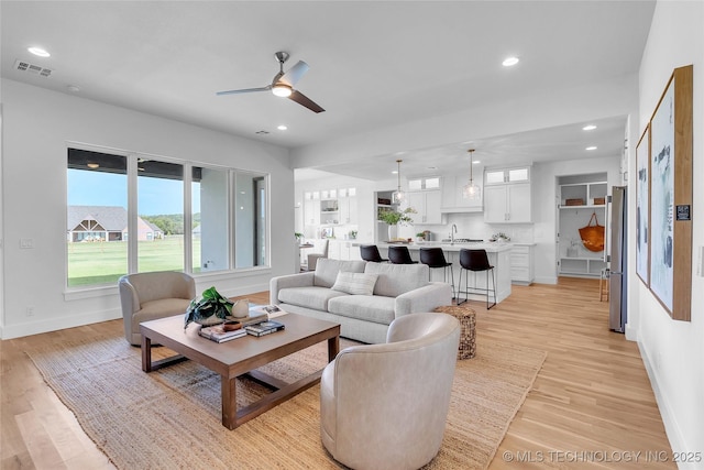 living room with sink, ceiling fan, and light hardwood / wood-style flooring