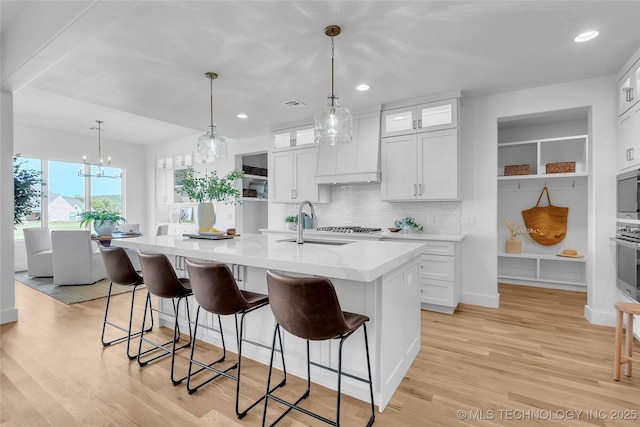 kitchen featuring sink, tasteful backsplash, an island with sink, white cabinets, and custom range hood