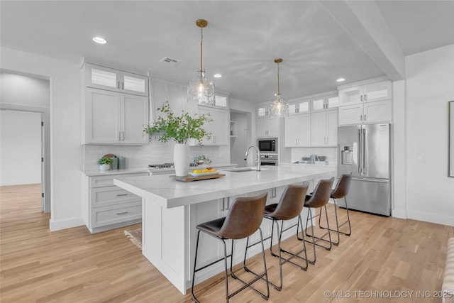 kitchen with stainless steel appliances, an island with sink, white cabinets, and light wood-type flooring