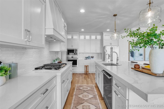 kitchen with sink, custom exhaust hood, hanging light fixtures, stainless steel appliances, and white cabinets