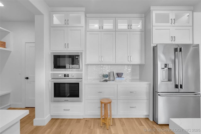 kitchen with tasteful backsplash, light stone counters, appliances with stainless steel finishes, light hardwood / wood-style floors, and white cabinets