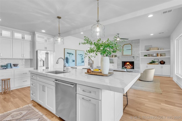 kitchen featuring sink, white cabinetry, decorative light fixtures, appliances with stainless steel finishes, and an island with sink