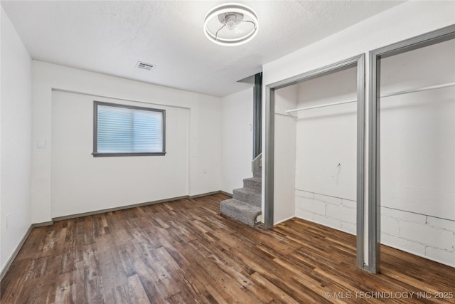 unfurnished bedroom featuring two closets, dark wood-type flooring, and a textured ceiling