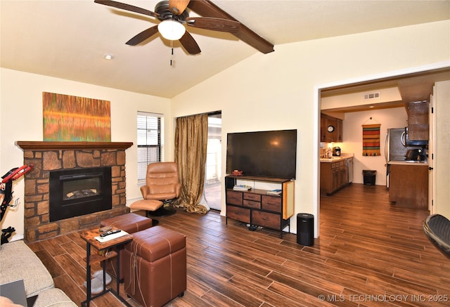 living room featuring lofted ceiling with beams, a stone fireplace, dark wood-type flooring, and ceiling fan