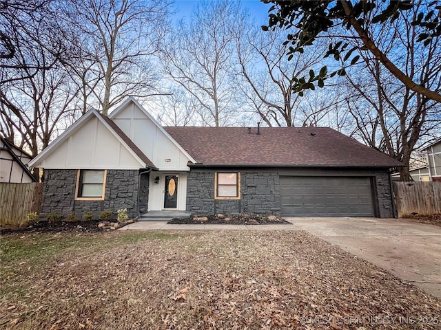 view of front of property featuring roof with shingles, an attached garage, fence, stone siding, and driveway