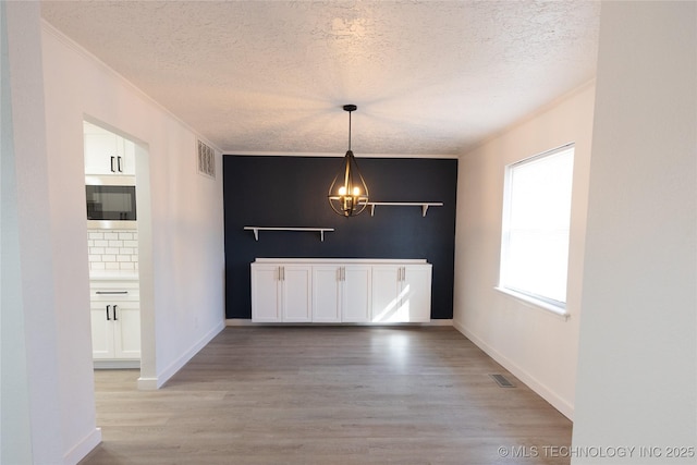 7850 S Park Ave, Broken Arrow, OK 74011 - unfurnished dining area with a textured ceiling, light wood-style floors, a chandelier, ornamental molding, and baseboards