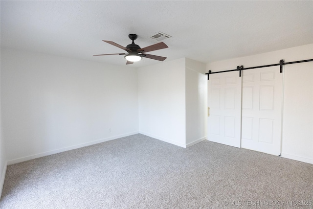 unfurnished bedroom with ceiling fan, carpet, a textured ceiling, a barn door, and a closet