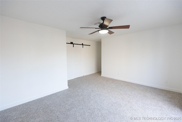 spare room featuring a barn door, baseboards, a ceiling fan, and carpet flooring