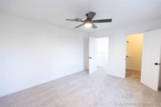 unfurnished bedroom with visible vents, a spacious closet, light carpet, ceiling fan, and baseboards