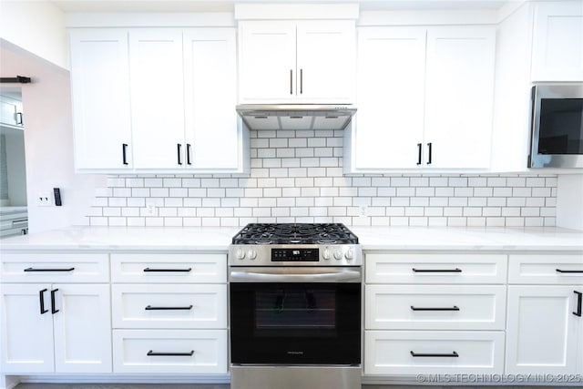 kitchen with light stone counters, stainless steel appliances, decorative backsplash, white cabinets, and under cabinet range hood