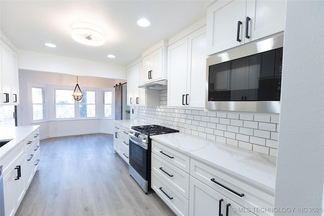 kitchen featuring hanging light fixtures, white cabinetry, appliances with stainless steel finishes, and light stone counters