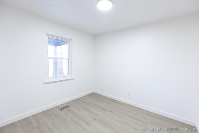 empty room with light wood finished floors, baseboards, and visible vents