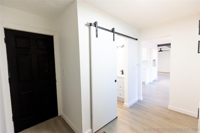 corridor with baseboards, light wood finished floors, and a barn door