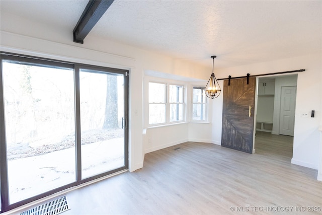 unfurnished dining area with hardwood / wood-style floors, a chandelier, a textured ceiling, a barn door, and beamed ceiling