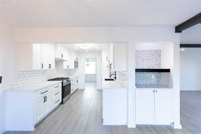 kitchen with white cabinets, light wood-style floors, stainless steel gas range oven, and light countertops