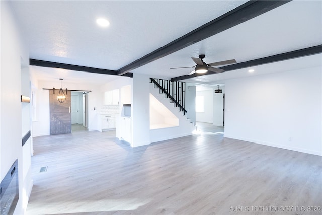 unfurnished living room with beamed ceiling, a barn door, light wood-type flooring, and a textured ceiling