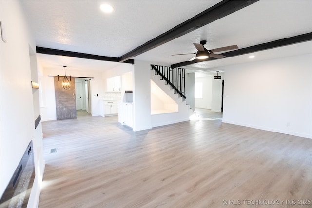 unfurnished living room featuring light wood-style flooring, beamed ceiling, stairs, a textured ceiling, and ceiling fan with notable chandelier