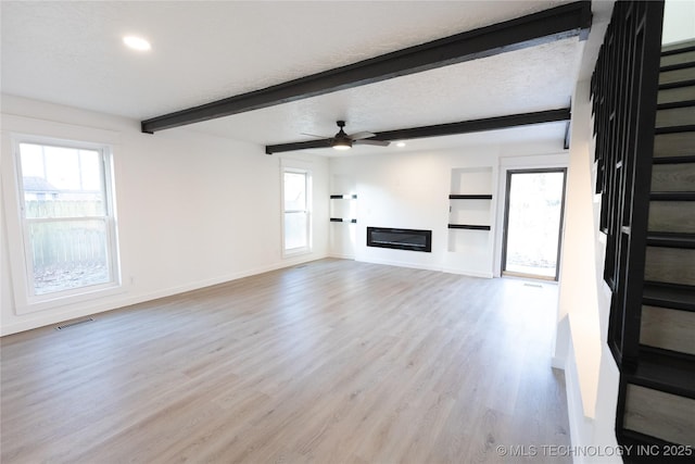 unfurnished living room featuring beam ceiling, ceiling fan, a textured ceiling, and light hardwood / wood-style floors