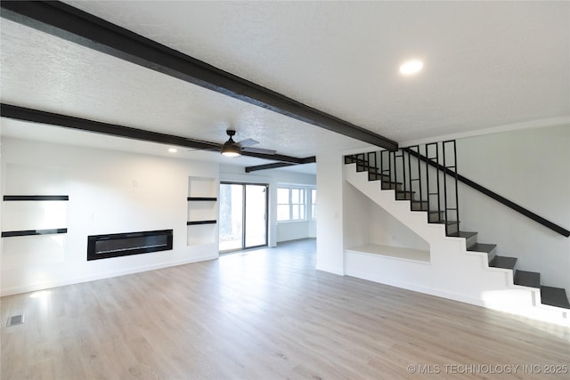 unfurnished living room with beamed ceiling, ceiling fan, light hardwood / wood-style floors, and a textured ceiling