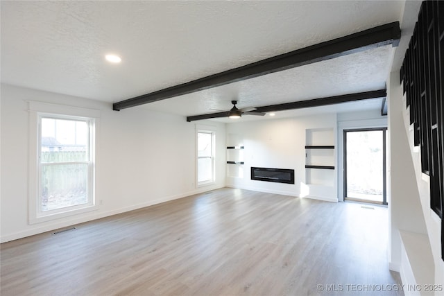 unfurnished living room with beam ceiling, plenty of natural light, a textured ceiling, and light wood-type flooring