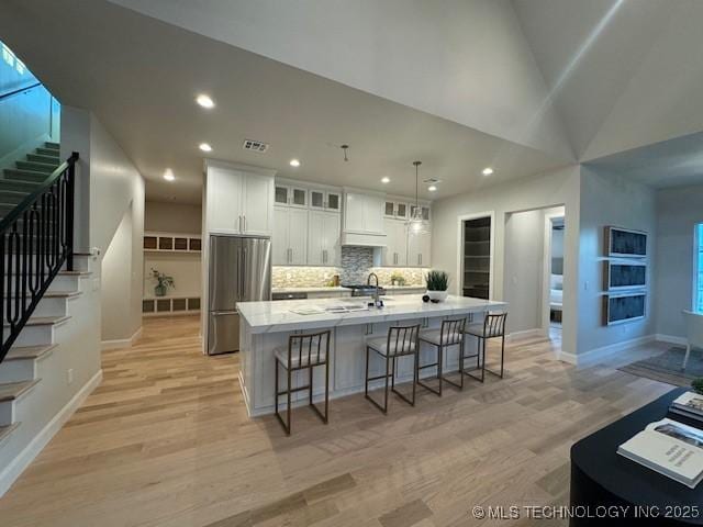 kitchen with stainless steel fridge, a kitchen island with sink, a breakfast bar area, and white cabinets