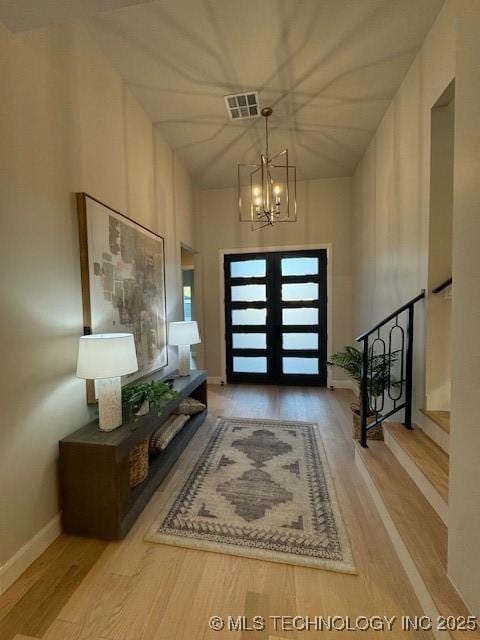 entryway featuring french doors, a high ceiling, light hardwood / wood-style flooring, and a notable chandelier