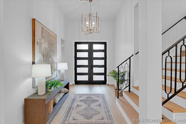 entrance foyer featuring french doors, light hardwood / wood-style floors, a high ceiling, and a notable chandelier