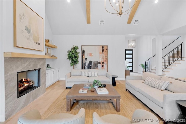 living room with an inviting chandelier, a high end fireplace, high vaulted ceiling, and light hardwood / wood-style flooring