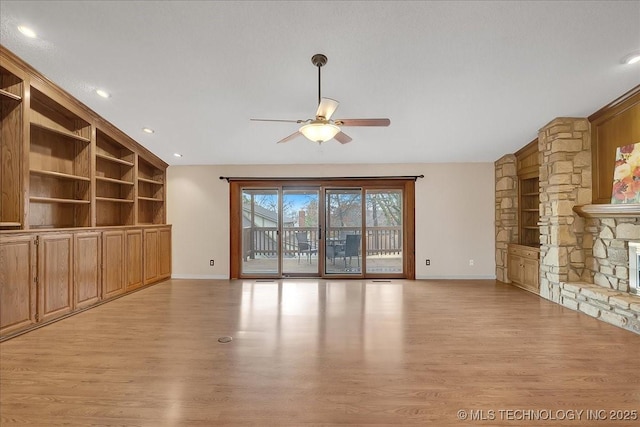 unfurnished living room with vaulted ceiling, built in features, ceiling fan, a fireplace, and light hardwood / wood-style floors