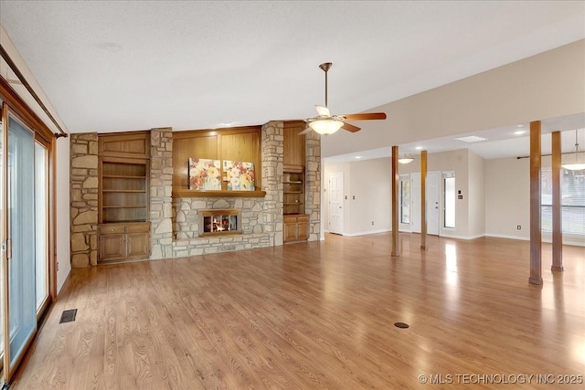 unfurnished living room with built in shelves, a stone fireplace, light hardwood / wood-style flooring, ceiling fan, and decorative columns