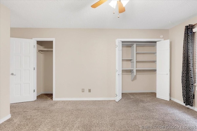 unfurnished bedroom with ceiling fan, two closets, light carpet, and a textured ceiling