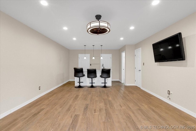 kitchen with hanging light fixtures, a kitchen island, light wood-type flooring, and a kitchen bar