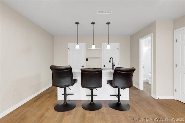 kitchen featuring hanging light fixtures, sink, a breakfast bar area, and light hardwood / wood-style flooring