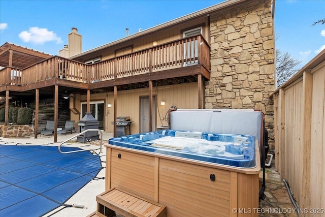 back of property featuring a wooden deck, a hot tub, and a patio area