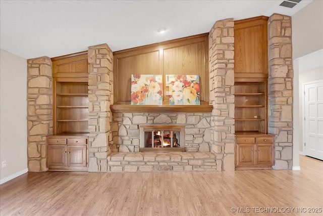 unfurnished living room with a stone fireplace, vaulted ceiling, light hardwood / wood-style floors, and built in shelves