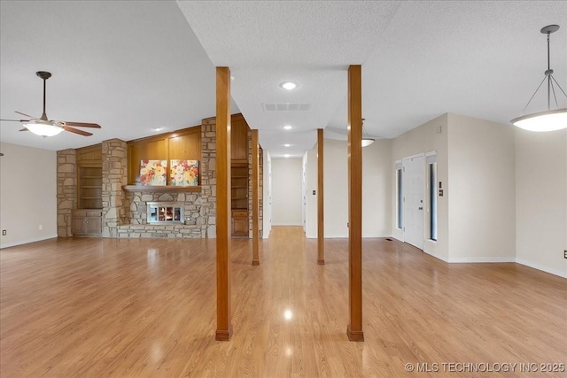 unfurnished living room with ceiling fan, a stone fireplace, light hardwood / wood-style flooring, and a textured ceiling