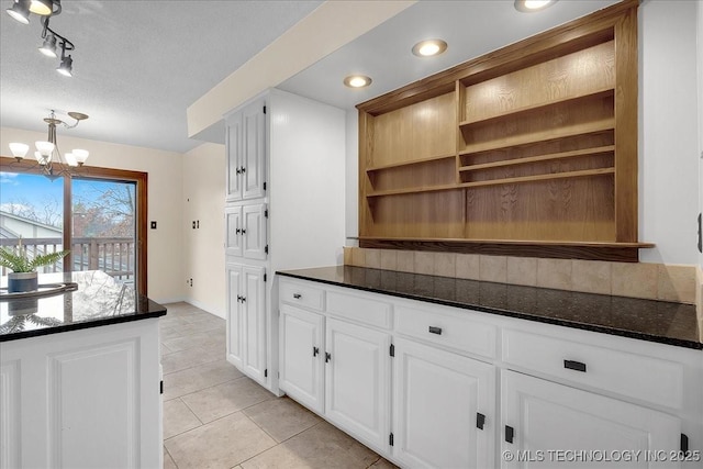 kitchen with white cabinetry, dark stone counters, light tile patterned floors, a notable chandelier, and a textured ceiling