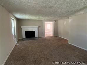 unfurnished living room featuring a textured ceiling and dark colored carpet