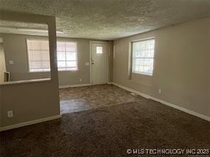 interior space with a healthy amount of sunlight, a textured ceiling, and dark carpet