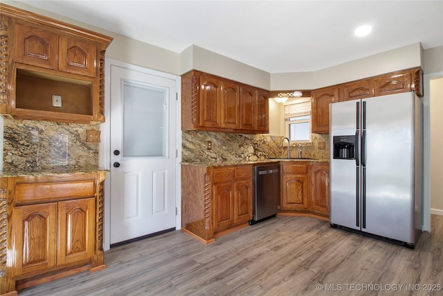 kitchen featuring refrigerator with ice dispenser, sink, light hardwood / wood-style flooring, light stone countertops, and stainless steel dishwasher