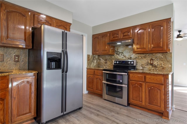 kitchen featuring stainless steel appliances, light stone countertops, light hardwood / wood-style flooring, and backsplash