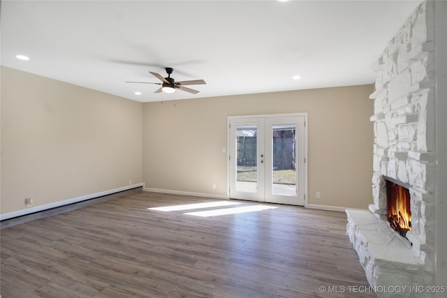 unfurnished living room with hardwood / wood-style flooring, a stone fireplace, french doors, and ceiling fan