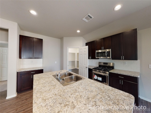 kitchen with appliances with stainless steel finishes, a kitchen island with sink, sink, and dark brown cabinets