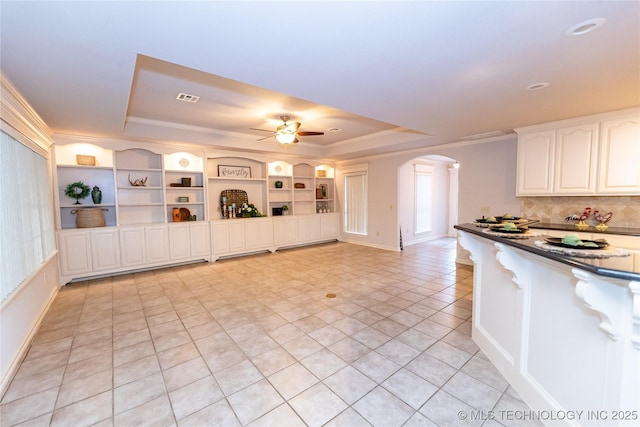 kitchen with ceiling fan, white cabinetry, backsplash, ornamental molding, and a raised ceiling