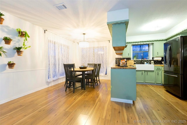 kitchen with green cabinetry, sink, black fridge with ice dispenser, and light hardwood / wood-style flooring