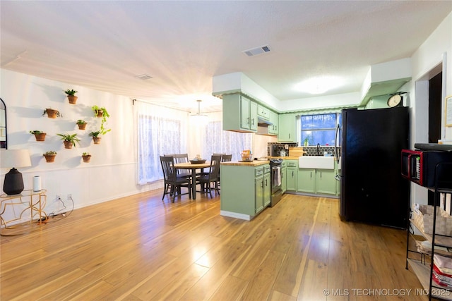 kitchen featuring sink, stainless steel electric range oven, refrigerator, light hardwood / wood-style flooring, and green cabinets