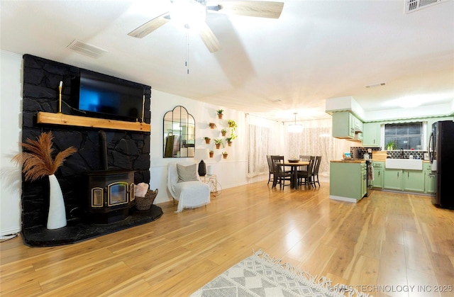 living room with ceiling fan, sink, a wood stove, and light wood-type flooring