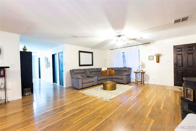 living room featuring light hardwood / wood-style flooring, ceiling fan, and a wood stove