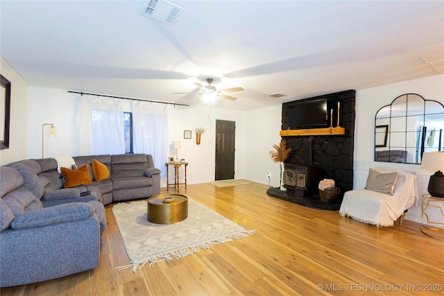 living room featuring a healthy amount of sunlight, a wood stove, hardwood / wood-style floors, and ceiling fan