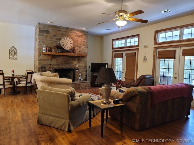 living room featuring hardwood / wood-style flooring, ceiling fan, a stone fireplace, and french doors